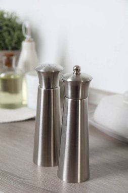 Metal salt and pepper mills on grey wooden counter indoors, closeup