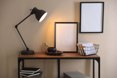 Stylish lamp, other decor and books on console table near beige wall indoors