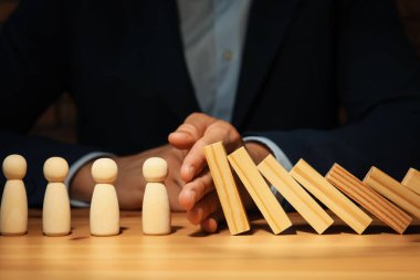 Risk. Tahta masada insan figürlerini domino etkisinden koruyan adam, yakın plan.