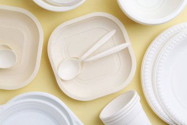 Soluk sarı zemin üzerinde tek kullanımlık plastik sofra takımı, düz yatıyordu.