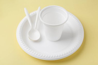 Soluk sarı arkaplanda tek kullanımlık plastik sofra takımı, yakın plan.
