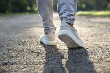 Havalı spor ayakkabılı bir adam asfaltta yürüyor, yakın plan.
