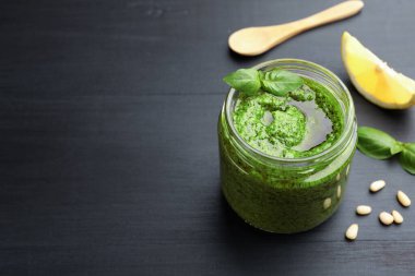 Kavanozda taze pesto sosu, siyah ahşap masada kaşık ve malzemeler, yakın plan. Metin için boşluk