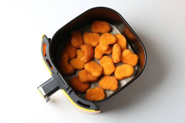 Air fryer basket with chicken nuggets on white background, top view
