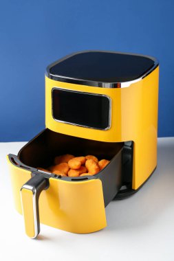 Air fryer with chicken nuggets on white table against blue background