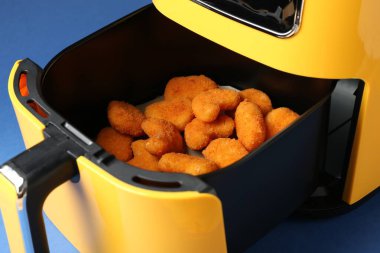 Mavi arka planda tavuk nugget 'ı olan bir kızartma makinesi, yakın plan.