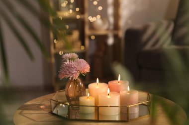 Yanan mumlarla dolu bir tepsi ve kapalı bir masa üzerinde güzel çiçekler, yakın plan. Bokeh etkisi