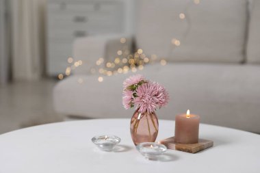 Burning candles and beautiful flowers on white table indoors, closeup with space for text. Bokeh effect