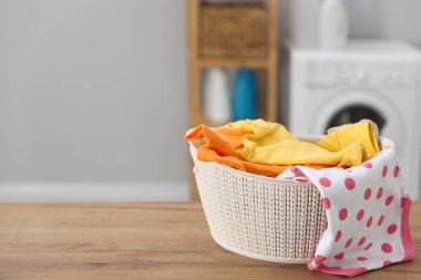 Laundry basket with clean baby clothes on wooden table indoors. Space for text