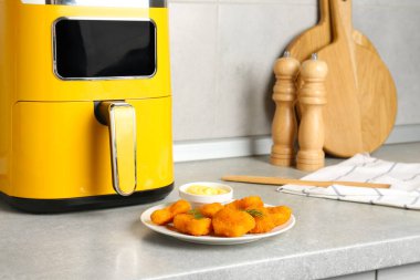 Tasty chicken nuggets with sauce near air fryer on light grey table