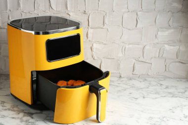Air fryer container with cooked chicken nuggets on white marble table, closeup. Space for text