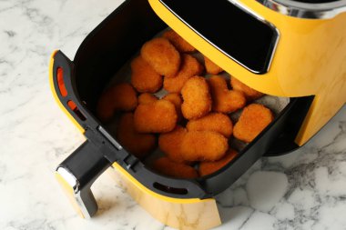 Air fryer container with cooked chicken nuggets on white marble table, above view