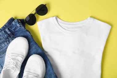 White t-shirt, jeans, sunglasses and sneakers on yellow background, flat lay. Mockup for design