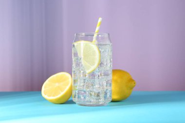 Refreshing lemon water with ice in glass and fresh citrus fruits on color background