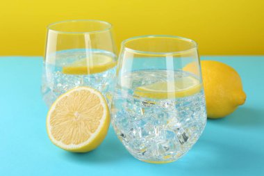 Refreshing lemon water with ice in glasses and fresh citrus fruits on color background, closeup