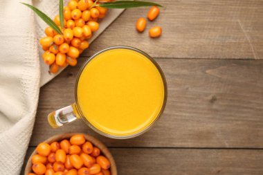 Cup of sea buckthorn tea and fresh berries on wooden table, flat lay. Space for text