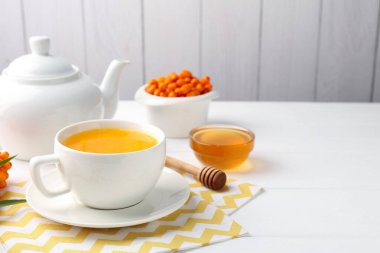 Sea buckthorn tea in cup, honey and fresh berries on white wooden table. Space for text