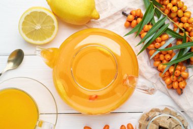 Sea buckthorn tea, fresh berries, sugar cubes and lemons on white wooden table, flat lay