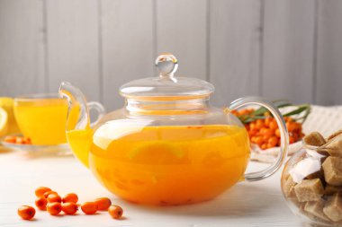Sea buckthorn tea, fresh berries and sugar cubes on white wooden table, closeup