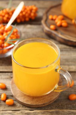 Sea buckthorn tea in cup and fresh berries on wooden table, closeup