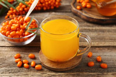 Sea buckthorn tea in cup and fresh berries on wooden table, closeup