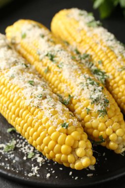 Tasty grilled corncobs with parsley and cheese on black table, closeup