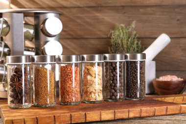 Farklı baharatlar cam kavanozlarda ve ahşap masada, yakın plan.