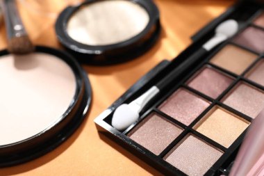 Colorful eyeshadow palette, powder and makeup applicator on orange background, closeup