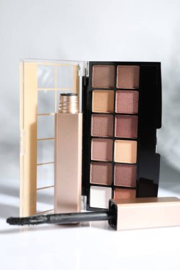 Eyeshadow palette and mascara on mirror surface against white background