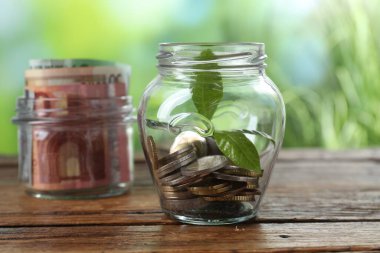 Bozuk paralarla dolu cam kavanoz ve ahşap masanın üzerinde bulanık arka plan, yakın plan