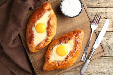 Tasty khachapuris with cheese and eggs served on wooden table, flat lay