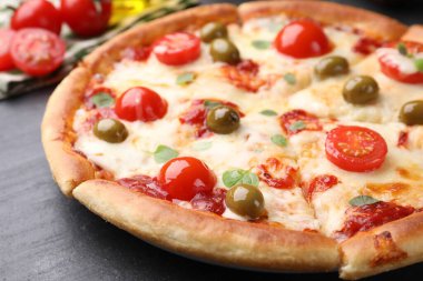 Peynirli, domatesli ve zeytinli lezzetli pizza koyu gri masada, yakın plan.