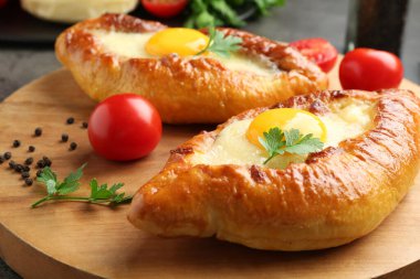 Tasty khachapuris with cheese, eggs, tomatoes and spices on grey table, closeup