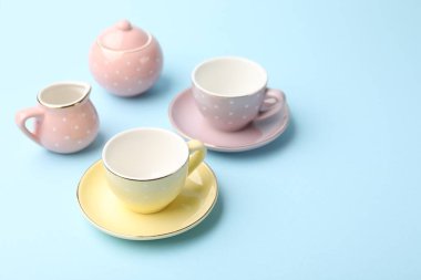 Beautiful ceramic tea set for children on light blue background, closeup. Space for text