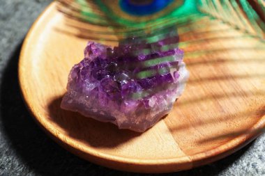 Gri masada güzel ametist taşı ve tavus kuşu tüyü, yakın plan.
