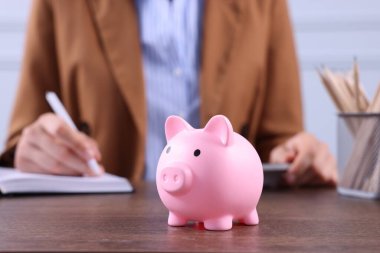 Domuz kumbarası ahşap masa ve kadın kapalı alanda çalışıyor, seçici odaklanma