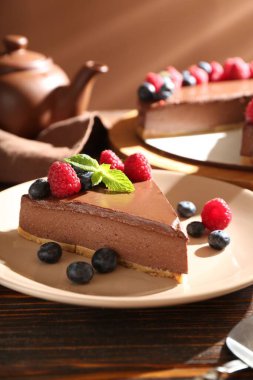 Tahta masada servis edilen meyveli çikolatalı cheesecake, yakın plan.