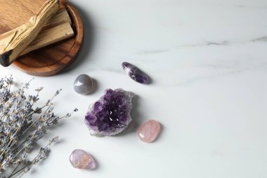 Different beautiful gemstones, palo santo and lavender flowers on white marble table, flat lay. Space for text