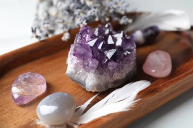 Different beautiful gemstones, feather and lavender flowers on white table, closeup