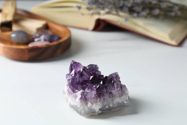 Different beautiful gemstones, book and lavender flowers on white table, closeup