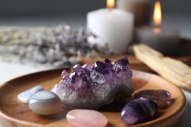 Different beautiful gemstones, palo santo, lavender flowers and burning candles on table, closeup