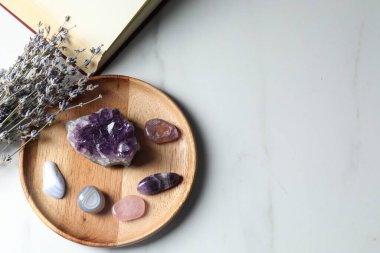 Farklı güzel değerli taşlar, kitap ve lavanta çiçekleri beyaz mermer masada, düz yerde. Metin için boşluk