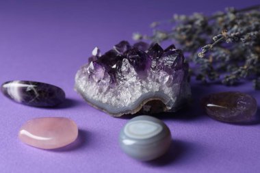 Beautiful amethyst gemstone and lavender flowers on purple background, closeup