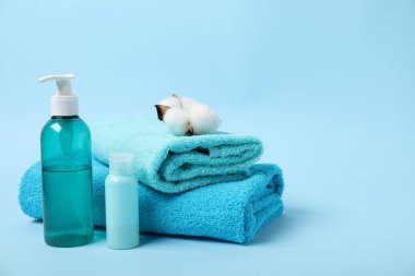 Fresh terry towels, personal hygiene products and cotton flower on light blue background. Space for text