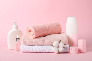 Bir yığın taze havlu, kozmetik ürünler ve pembe arka planda pamuk.