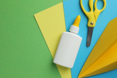 Şişedeki yapıştırıcı, makas, renkli kağıt ve yeşil arka planda el yapımı uçak, düz yatak. Metin için boşluk