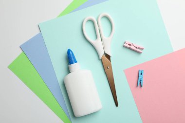 Beyaz arkaplanda yapıştırıcı, makas, ataç ve renkli kağıt düz konum