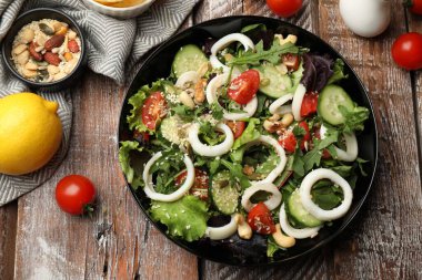 Delicious squid salad and ingredients on wooden table, flat lay