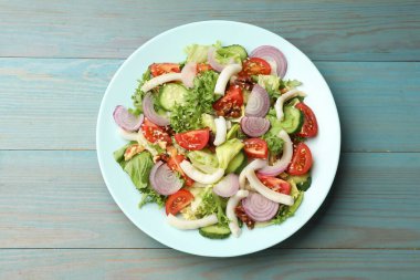 Açık mavi ahşap masada kalamar, sebze ve ceviz ile nefis bir salata.