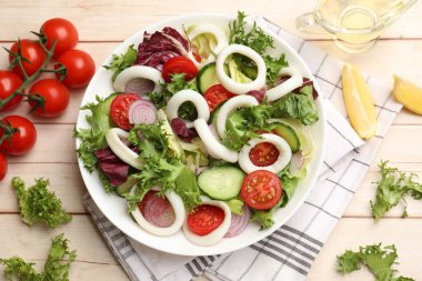 Delicious salad with squid rings and vegetables served on light wooden table, flat lay